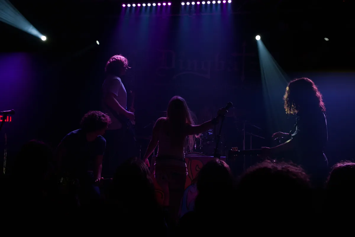 Dingbatz under a violet and blue wash, the band spread across the stage with the singer at the mic and the heads of the crowd silhouetted along the bottom of the frame